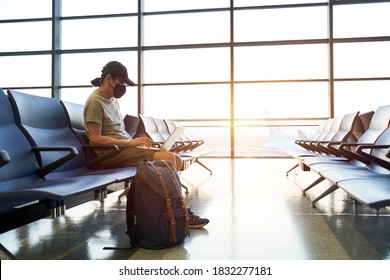 Asian Man Male Air Traveler With Black Face Mask Sitting In Emply Waiting Area In Airport Terminal Building Using Laptop Computer