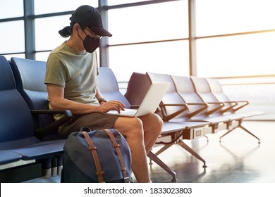 Asian Man Male Air Traveler With Black Face Mask Sitting In Emply Waiting Area In Airport Terminal Building Using Laptop Computer