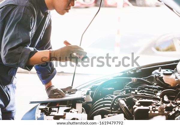 Asian Man\
mechanic inspection Shine a torch car engine checking bug in\
engine.Blue car for service maintenance insurance with car\
engine.for transport automobile\
automotive