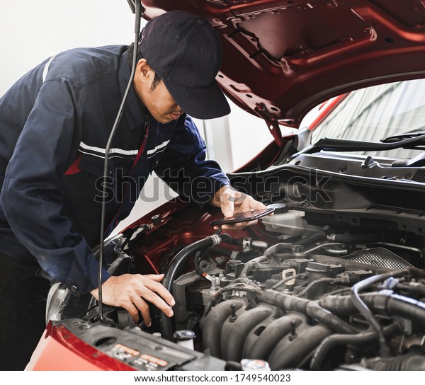 Asian Man mechanic inspection Shine a torch\
car engine checking bug in engine from application smartphone.Red\
car for service maintenance insurance with car engine.for transport\
automobile automotive