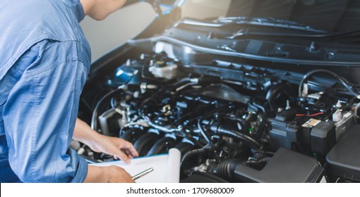 Asian Man mechanic inspection writing note on clipboard.Blue car for service maintenance insurance with car engine.for transport automobile automotive image.