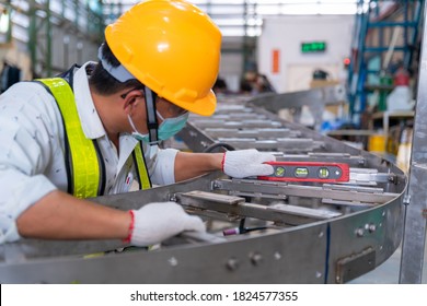 Asian Man Mechanic Wearing Protective Mask To Protect Against Covid-19,male Technician Worker Use A Water Level Meter Working And Assemble The Product Sorting Machine Conveyer In Industrial Factory.