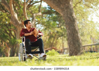 Asian Man On Wheelchair Ride On The Garden And Reading A Book.