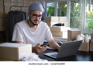 Asian man online seller confirming orders from customer on the phone. E-commerce male business owner looking at the phone in store warehouse. - Shutterstock ID 2146956989