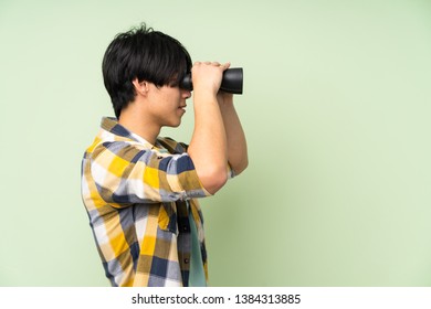 Asian Man Over Isolated Green Wall With Black Binoculars