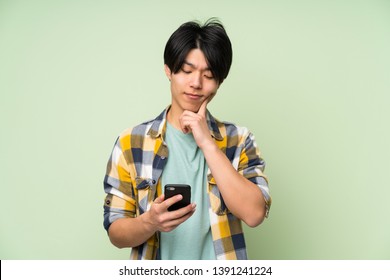 Asian Man Over Isolated Green Wall Using Mobile Phone