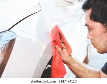 An Asian man owns a car wiping and cleaning the body paint of a car with a red cloth