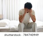 asian man painful and miserable sitting on bed head down covering face with hands.