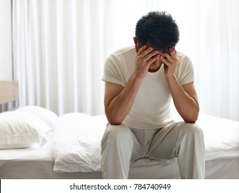 Asian Man Painful And Miserable Sitting On Bed Head Down Covering Face With Hands.