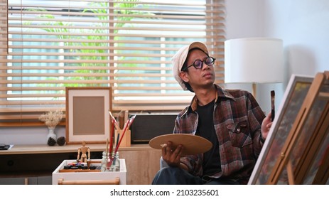 Asian Man Painting Picture On Canvas With Oil Paints At Art Studio.