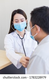 Asian Man Patient Are Checked Up His Health While A Woman Doctor Use A Stethoscope To Hear Heart Rate Of Hims In Coronavirus Pandemic By Wearing A Surgical Mask At All Times. Coronavirus Protection.