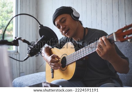 Asian man performancing music and singing with microphone at home sound recording studio. Man plays guitar and sing a song. 