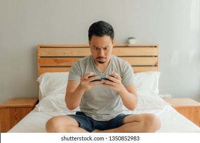 Asian Man Is Playing Mobile Game With His Smartphone On The Bed.