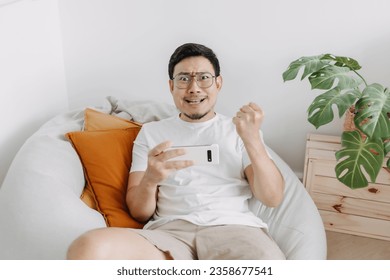 Asian man playing mobile game making funny intense face in the living room.