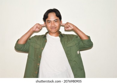 Asian Man Pose Covering Ears With Smiling Face. Illustration Of Ignorant, Whatever, Don't Care. Portrait Of Indonesian People On White Background Isolated