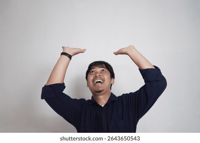 Asian man posing as if something has fallen on him. Raising both hands up. The man is wearing a casual navy long-sleeved shirt with his sleeves rolled up.