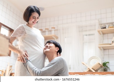 Asian man and pregnancy woman stand in kitchen at home. Father holding mother tummy listen & hear infant inside mom belly. Husband sits and hugs wife. Love and care of pregnant and newborn kid concept - Powered by Shutterstock