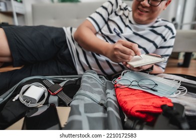 Asian Man Is Preparing Clothes In Suitcases. He's Choosing Clothes, Travel Documents, The Itinerary For A Solo Trip, And Check The Checklist. Travel, Holiday And Vacation Concept.