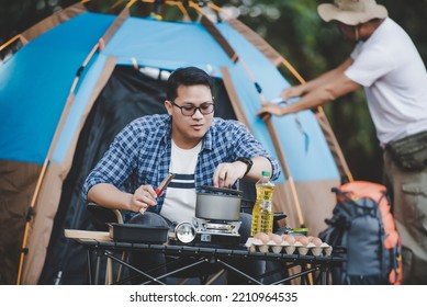 Asian man preparing pitch a tent in camping while the other man was preparing food. in camping. Cooking set front ground. Outdoor cooking, traveling, camping, lifestyle concept. - Shutterstock ID 2210964535
