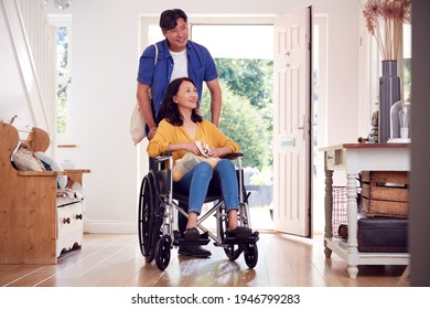 Asian Man Pushing Wife In Wheelchair At Home Back From Shopping Trip With Bag