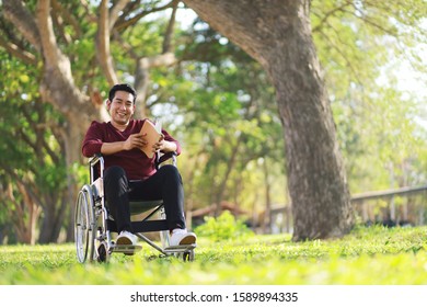 Asian Man Reading A Book On Wheelchair At The Garden.