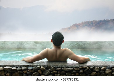 Asian Man Relaxing In Outdoor Hot Bath With Mountains View In Autumn.