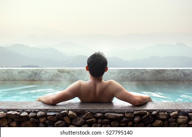 Asian Man Relaxing In Outdoor Hot Bath With Mountains View.