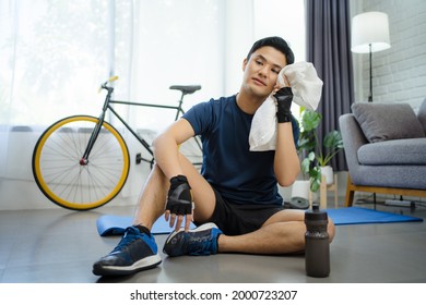 Asian Man Resting After Training. He Sits On The Floor At Home, Sport And Motivation Concept.