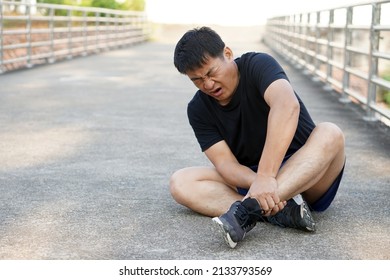 Asian Man Runner Gets Hurt On His Painful Ankle After Running , Jogging, Exercise. Concept : Injury Ankle Twist Sprain Accident In Workout Or Sport. Copy Space For Text.                