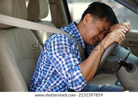 Asian man is sad and crying in car. His face down on the steering wheel. Concept :  Concept : Feeling and emotions. Sad, depressed  from health problems,   economic crisis, unemployed, brokenhearted. 