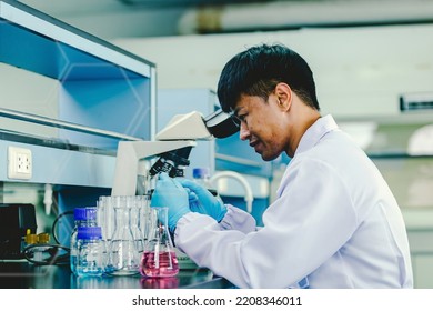 Asian Man Scientist  Looking Through Microscope In Laboratory Room.