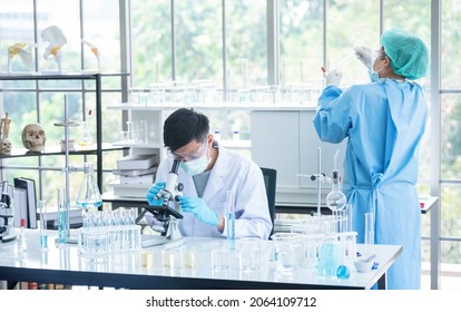 Asian Man Scientist Researcher Using Microscope In Laboratory. Medical Healthcare Technology And Pharmaceutical Research And Development Concept.