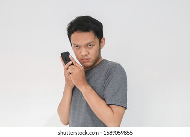 Asian Man Serious Face And Sharp Looking With Hiding The Phone Gesture Isolated Grey Background.