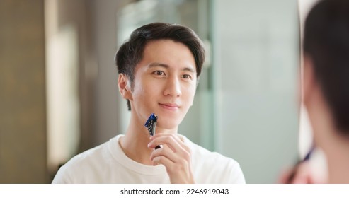 Asian man shaving in bathroom happily smiling to mirror - Powered by Shutterstock