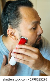 Asian Man Shaving Beard With Electric Razor Machine.