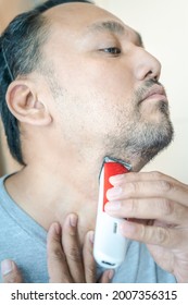 Asian Man Shaving Beard With Electric Razor Machine.