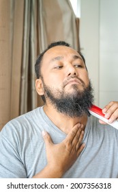 Asian Man Shaving Beard With Electric Razor Machine.