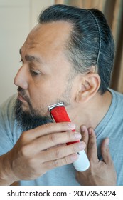 Asian Man Shaving Beard With Electric Razor Machine.