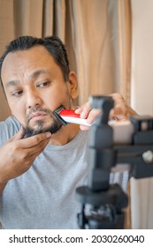 Asian Man Shaving Beard With Electric Razor Machine.