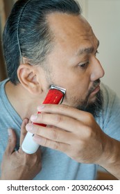 Asian Man Shaving Beard With Electric Razor Machine.