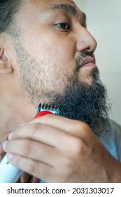 Asian Man Shaving Beard With Electric Razor Machine.