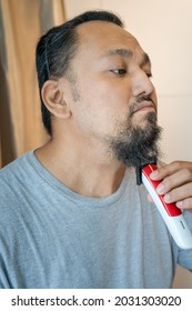 Asian Man Shaving Beard With Electric Razor Machine.