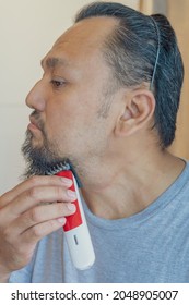 Asian Man Shaving Beard With Electric Razor Machine.