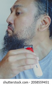 Asian Man Shaving Beard With Electric Razor Machine.