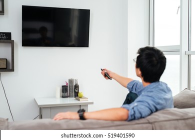 Asian Man In Shirt Watching Tv On Sofa. Back View