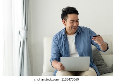 Asian Man Shopping Online With Holding Credit Card And Laptop And Sitting At Home, Lifestyle Concept.