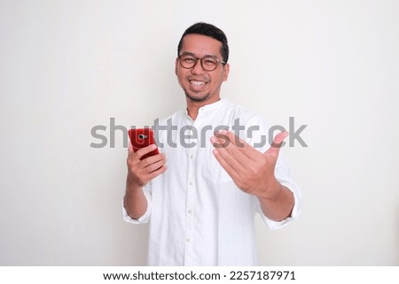 Asian man showing excited expression and doing inviting hand gesture while holding handphone