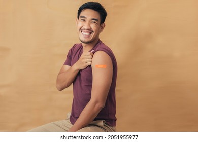 Asian Man Showing Shoulders After Getting A Vaccine. Happy Man Showing Arm With Band-aids On After Vaccine Injection.