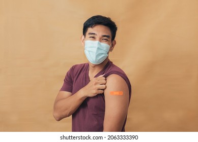 Asian Man Showing Shoulders After Getting A Vaccine. Happy Man Showing Arm With Band-aids On After Vaccine Injection.