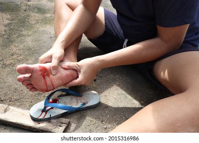 An Asian Man Shows A Foot Wound After Stepping On A Rusty Nail On A Wood. The Wound From The Foot Was Bleeding Profusely. It's Very Painful And Can Damage Nerves. It's Time For A Tetanus Shot.